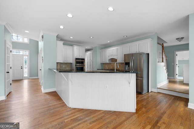 kitchen featuring a peninsula, ornamental molding, decorative backsplash, appliances with stainless steel finishes, and dark countertops