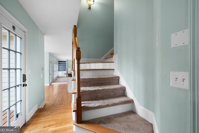 staircase featuring baseboards, a healthy amount of sunlight, and wood finished floors