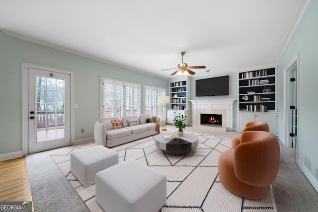 living room with built in shelves, ornamental molding, wood finished floors, a premium fireplace, and baseboards