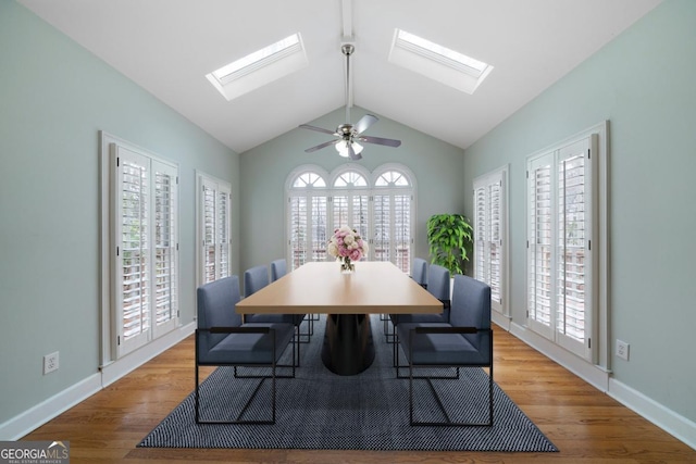 dining area featuring lofted ceiling with skylight, ceiling fan, baseboards, and wood finished floors