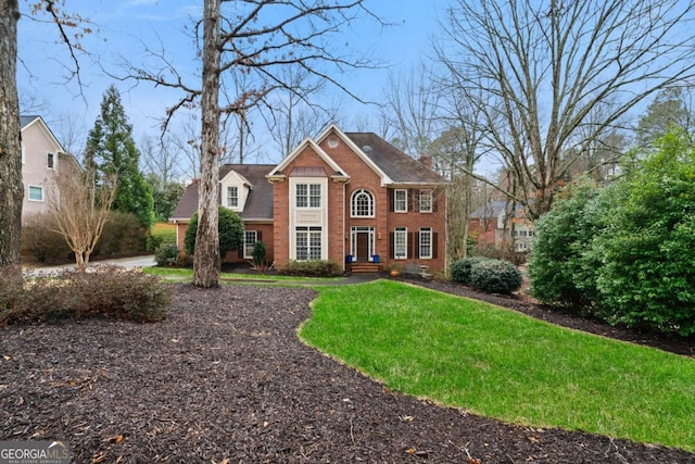 view of front facade featuring brick siding, a chimney, and a front yard