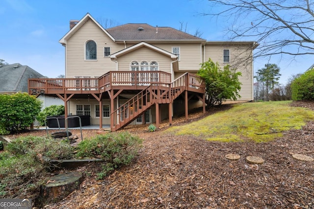 rear view of property featuring a hot tub, stairway, a wooden deck, a lawn, and a patio