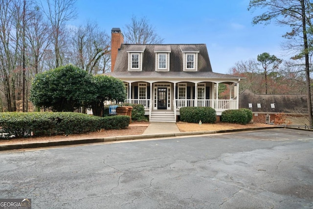 view of front facade featuring a porch, a chimney, and roof with shingles