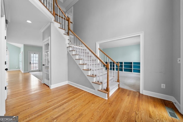 staircase with visible vents, a high ceiling, baseboards, and wood finished floors