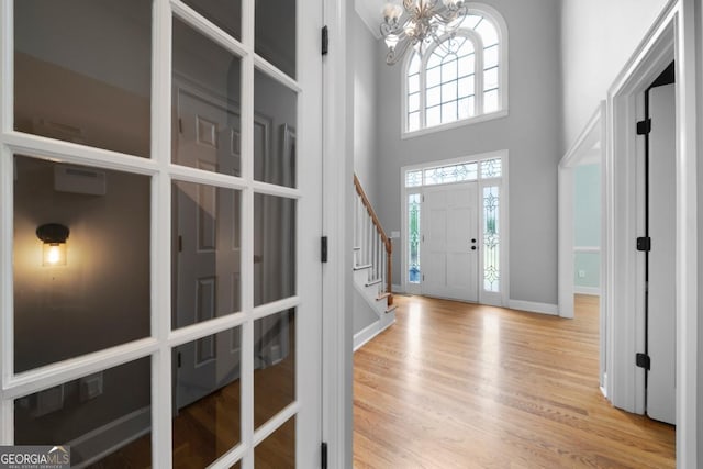 entrance foyer with wood finished floors, baseboards, an inviting chandelier, a high ceiling, and stairs