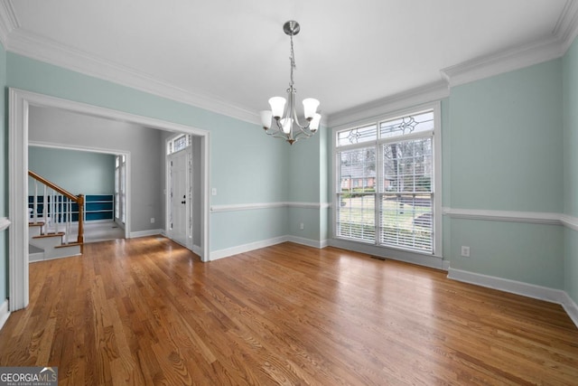 unfurnished room with wood finished floors, stairway, an inviting chandelier, crown molding, and baseboards