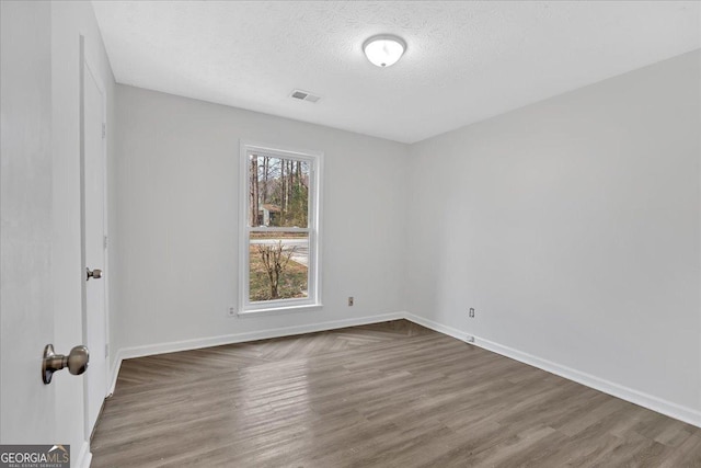 unfurnished room featuring a textured ceiling, wood finished floors, visible vents, and baseboards