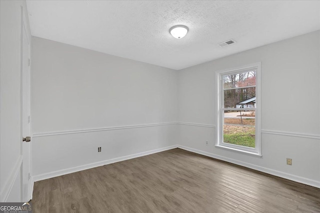 empty room featuring visible vents, a textured ceiling, a healthy amount of sunlight, and wood finished floors