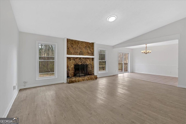 unfurnished living room featuring lofted ceiling, a stone fireplace, wood finished floors, and a healthy amount of sunlight