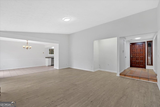 unfurnished living room featuring an inviting chandelier, wood finished floors, and baseboards