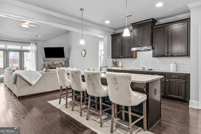 kitchen with under cabinet range hood, a kitchen breakfast bar, tasteful backsplash, and crown molding