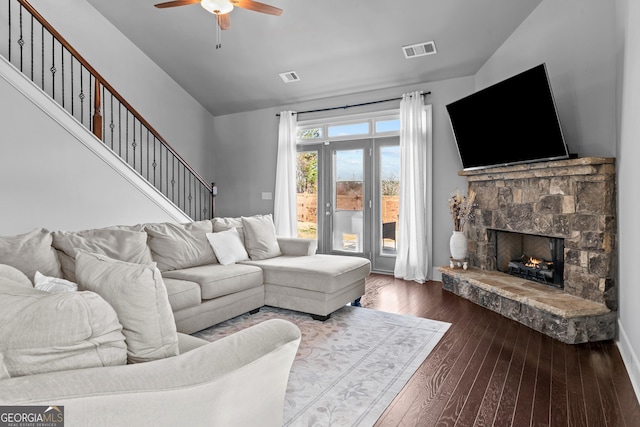 living area with visible vents, a stone fireplace, ceiling fan, and dark wood-style flooring