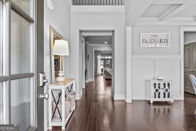 entrance foyer with dark wood finished floors, beam ceiling, a decorative wall, and ornamental molding