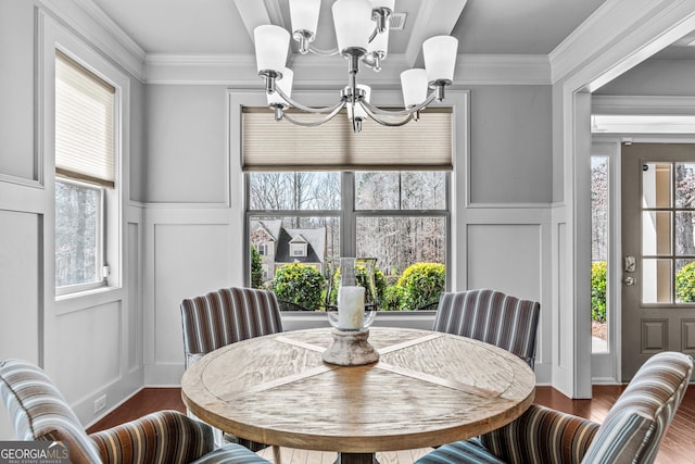 dining area with a healthy amount of sunlight, crown molding, an inviting chandelier, wood finished floors, and a decorative wall