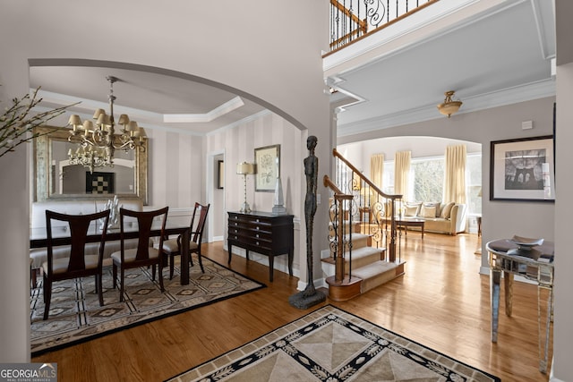 dining room with wood finished floors, an inviting chandelier, arched walkways, ornamental molding, and stairs