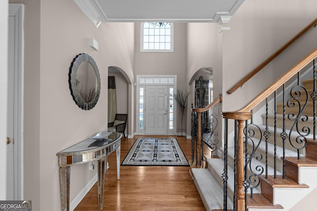 foyer entrance featuring wood finished floors, a high ceiling, crown molding, baseboards, and stairs