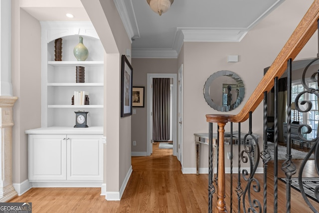 corridor with stairway, built in features, baseboards, light wood finished floors, and ornamental molding