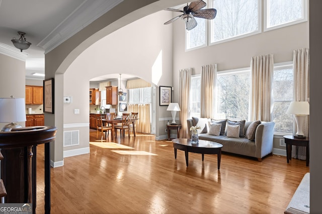 living room featuring light wood-style floors, arched walkways, visible vents, and ornamental molding