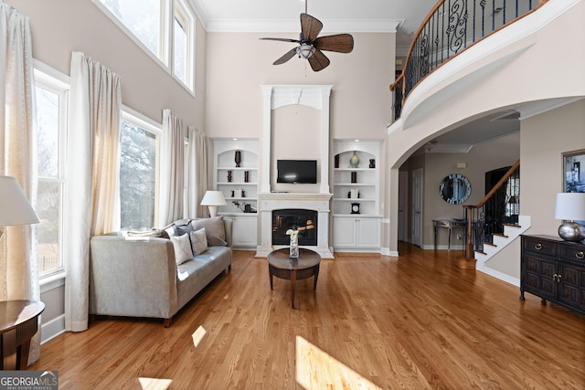 living area with wood finished floors, baseboards, arched walkways, ornamental molding, and a glass covered fireplace