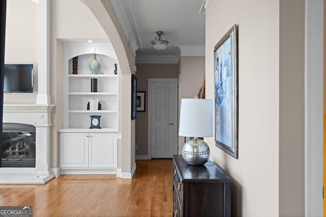 hallway with built in shelves, light wood-type flooring, and ornamental molding