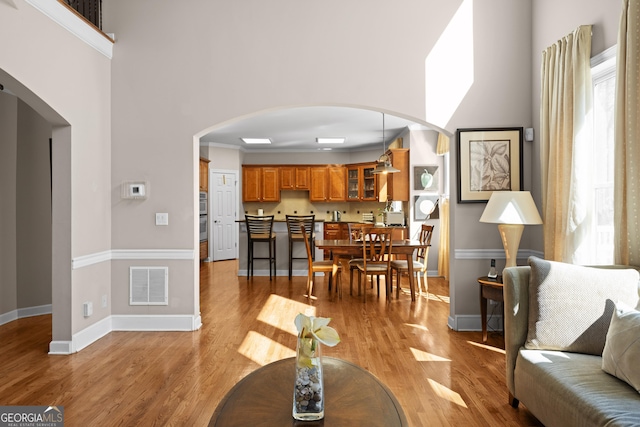 living room featuring light wood finished floors, visible vents, arched walkways, and a high ceiling