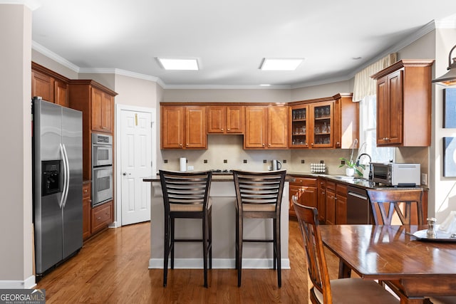 kitchen featuring wood finished floors, a toaster, appliances with stainless steel finishes, brown cabinets, and backsplash