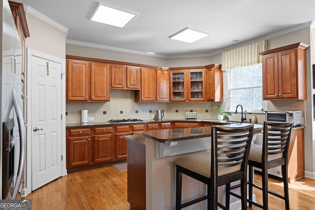 kitchen featuring a breakfast bar, stainless steel appliances, light wood-style floors, brown cabinetry, and crown molding