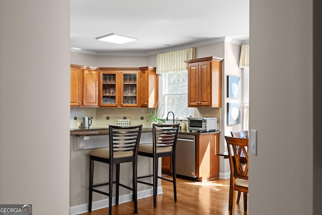 kitchen with tasteful backsplash, dishwasher, a breakfast bar area, brown cabinets, and wood finished floors