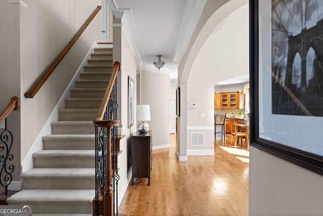 stairs featuring wood finished floors, visible vents, baseboards, arched walkways, and crown molding