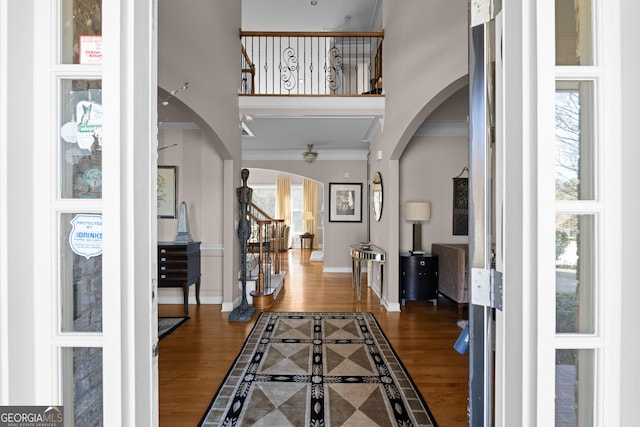 foyer entrance featuring plenty of natural light, wood finished floors, arched walkways, a high ceiling, and baseboards