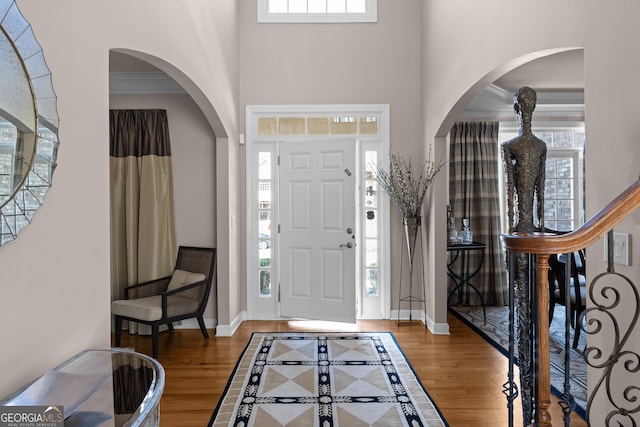 entryway featuring baseboards, stairs, ornamental molding, a high ceiling, and wood finished floors