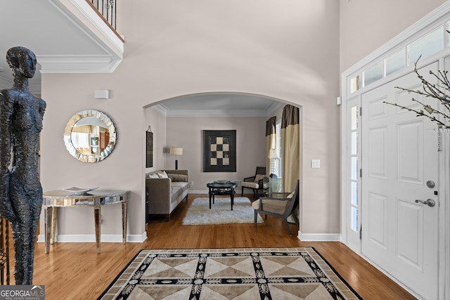 entrance foyer featuring baseboards, ornamental molding, a towering ceiling, wood finished floors, and arched walkways