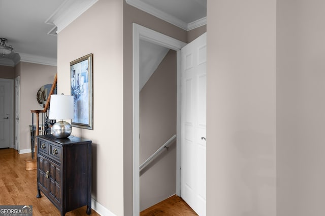 corridor featuring crown molding, light wood-style flooring, an upstairs landing, and baseboards