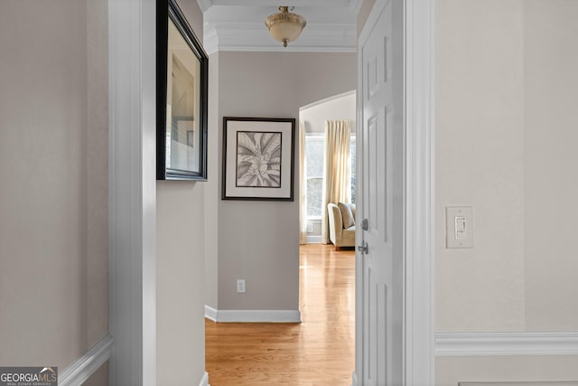 hall featuring light wood-type flooring, baseboards, and crown molding