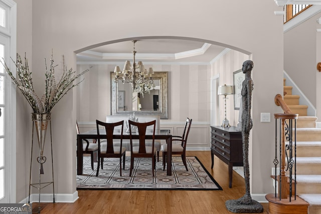 dining room with a raised ceiling, stairway, wood finished floors, and arched walkways