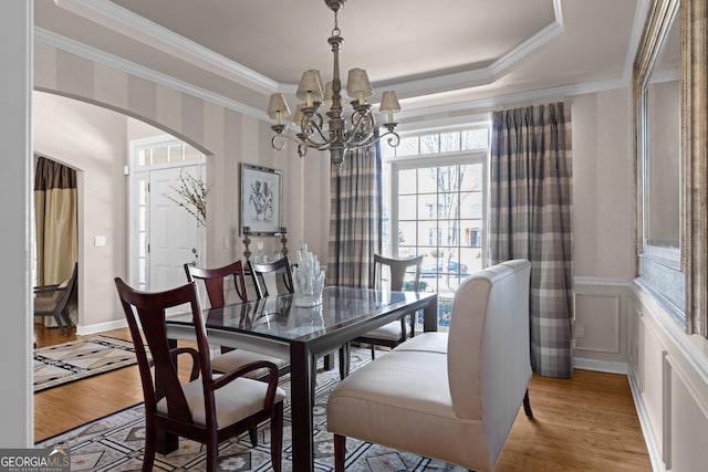 dining room with light wood-type flooring, arched walkways, an inviting chandelier, and ornamental molding