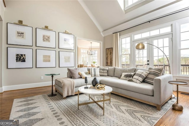 living area with wood finished floors, baseboards, high vaulted ceiling, an inviting chandelier, and ornamental molding