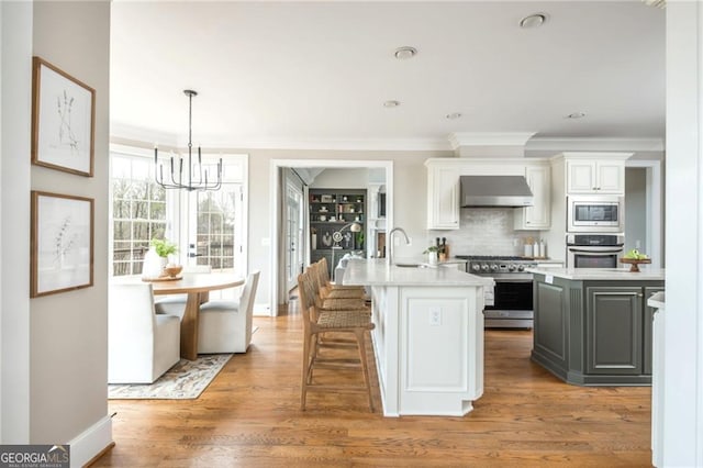 kitchen featuring a center island with sink, stainless steel appliances, extractor fan, light countertops, and light wood-type flooring