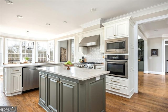 kitchen with a sink, light countertops, appliances with stainless steel finishes, wall chimney range hood, and a center island