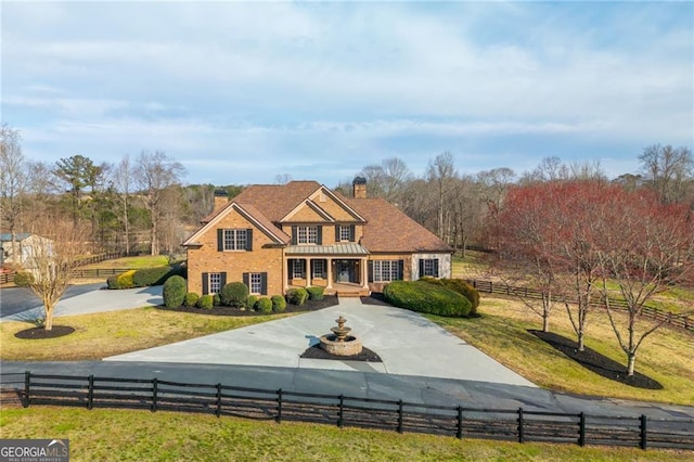 colonial-style house featuring driveway, a fenced front yard, and a chimney