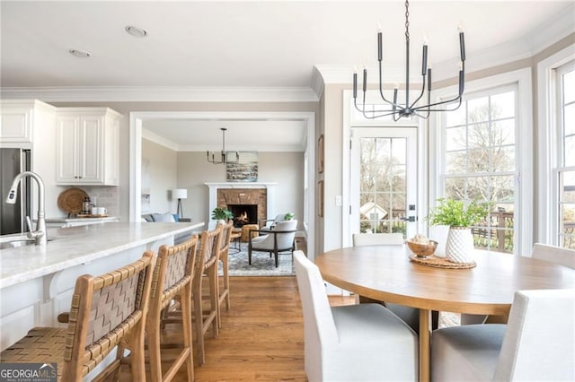 dining area with a fireplace, an inviting chandelier, light wood-style flooring, and crown molding