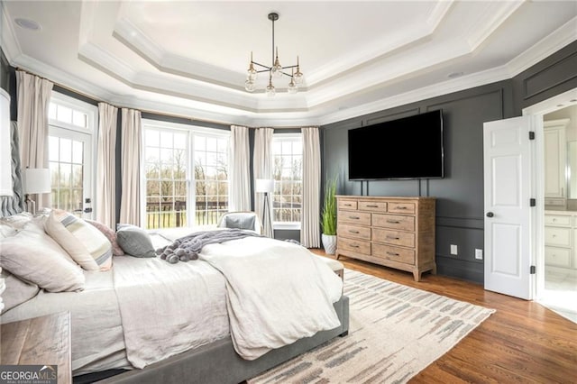 bedroom featuring a raised ceiling, an inviting chandelier, wood finished floors, and ornamental molding