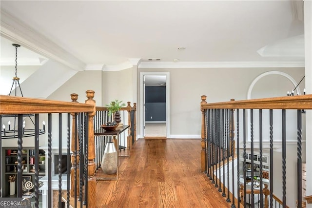 corridor featuring wood finished floors, baseboards, visible vents, ornamental molding, and a notable chandelier