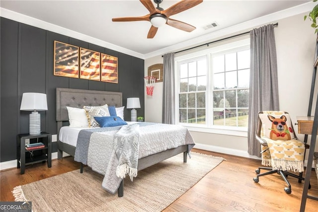 bedroom featuring visible vents, baseboards, wood finished floors, and crown molding