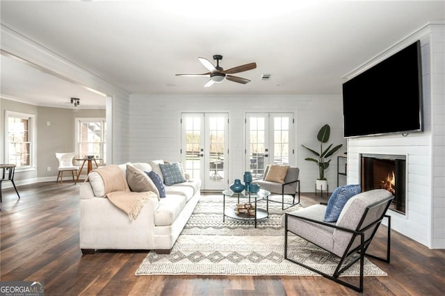 living area with wood finished floors, french doors, a warm lit fireplace, and ornamental molding