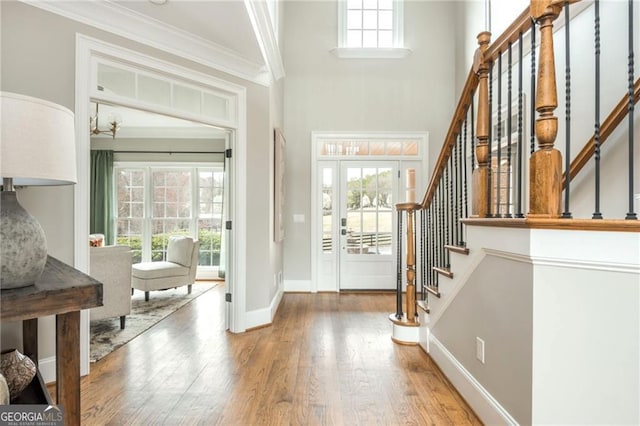 entryway featuring crown molding, baseboards, stairway, a towering ceiling, and wood finished floors