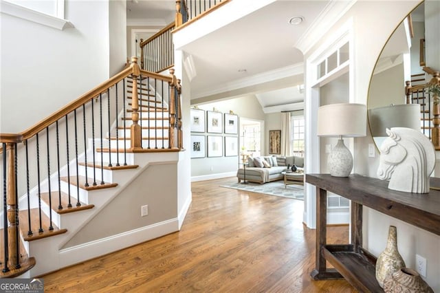 stairs with vaulted ceiling, wood finished floors, baseboards, and ornamental molding