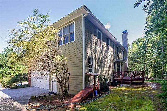 view of side of home featuring a deck, driveway, a chimney, and a garage