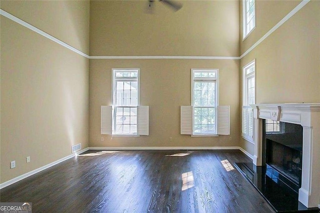 unfurnished living room with visible vents, baseboards, a fireplace with flush hearth, a high ceiling, and wood finished floors