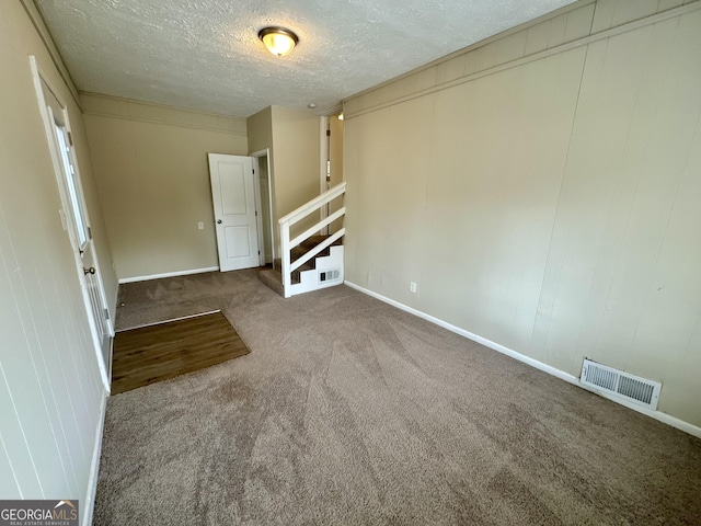 unfurnished room featuring visible vents, a textured ceiling, carpet, baseboards, and stairs